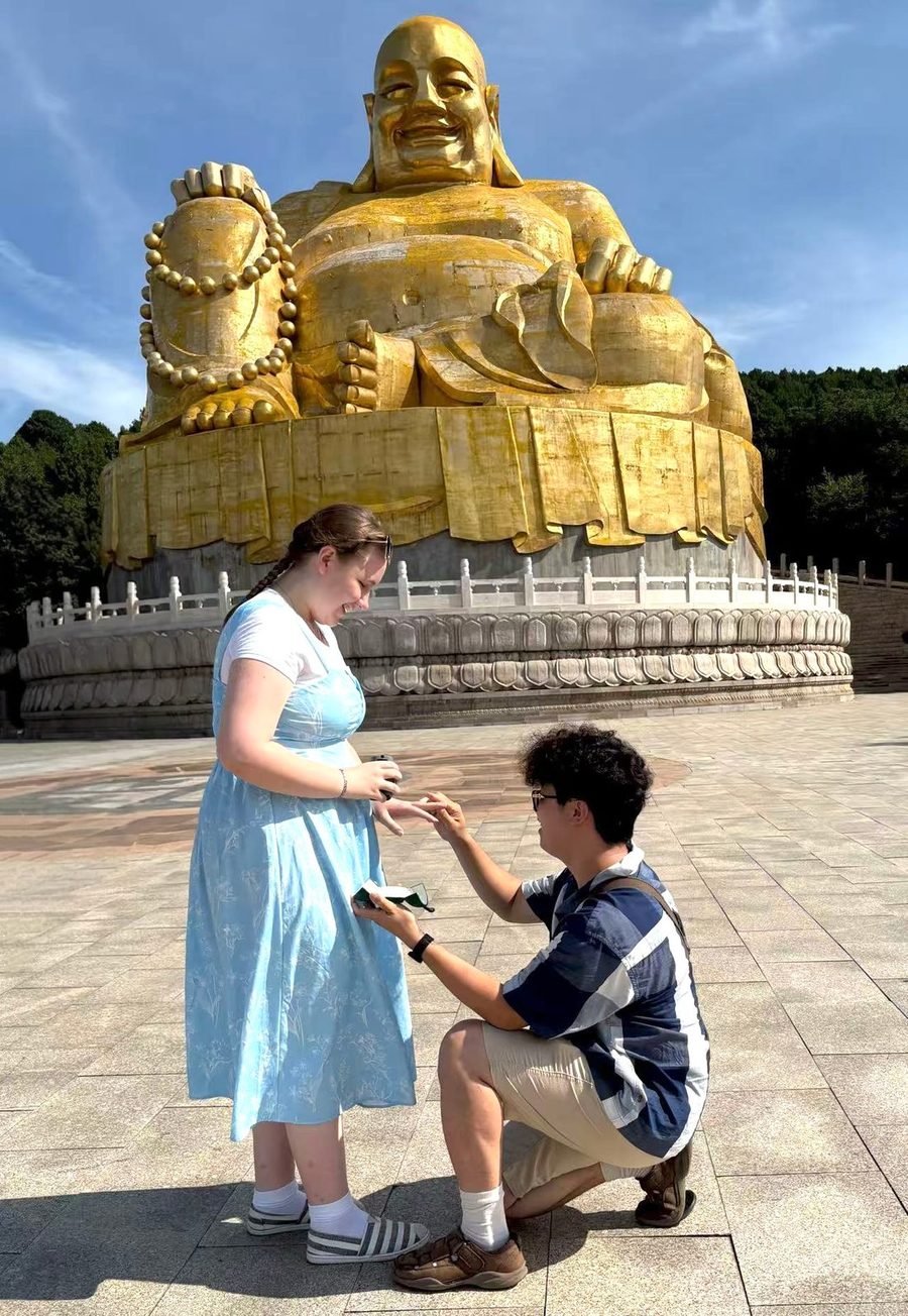 Tianli on one knee in front of the Maitreya Buddha at Qianfo Shan, Jinan, proposing to Jessie. The whole statue is visible above them.